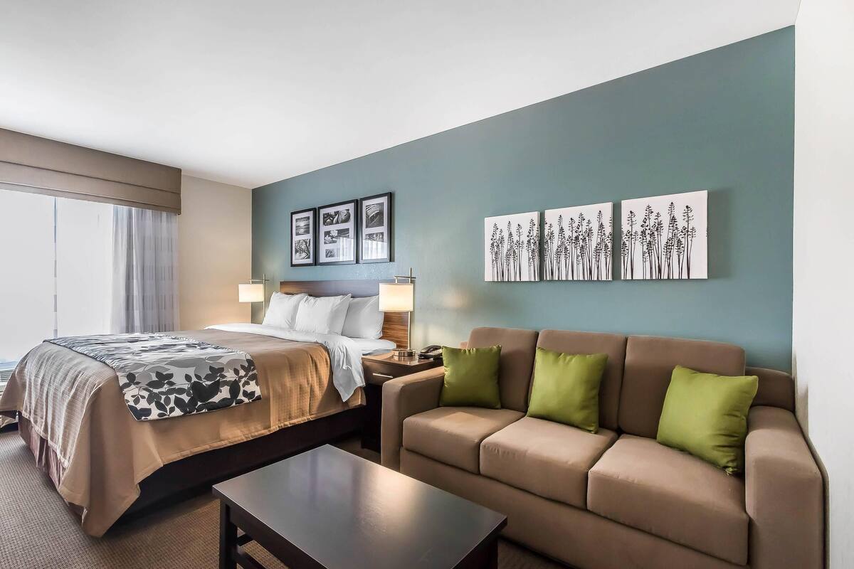 Quarto de hotel com cama, sofá, mesa de centro e obras de arte nas paredes.