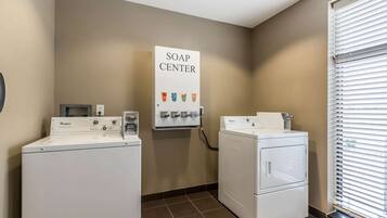 A laundry area with two Whirlpool washers and dryers, a soap dispenser, and a window with blinds.