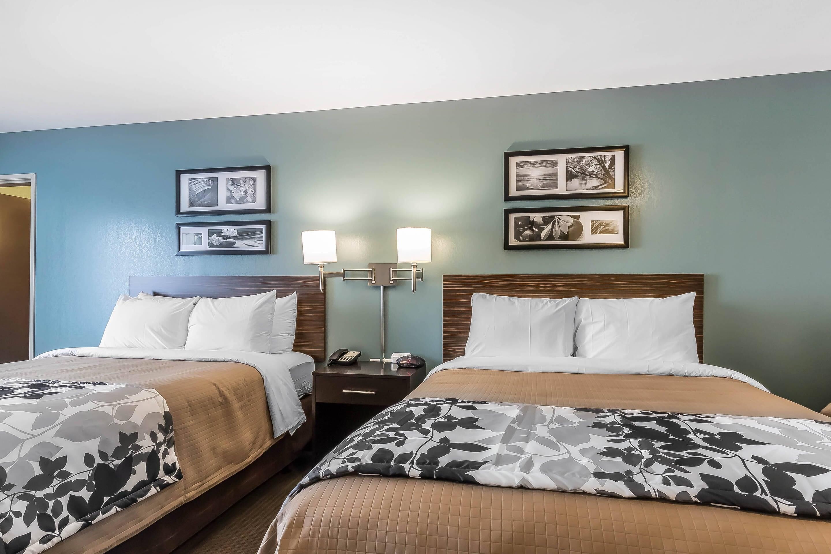 A hotel room with two beds, a nightstand with a lamp, and framed pictures on the wall.