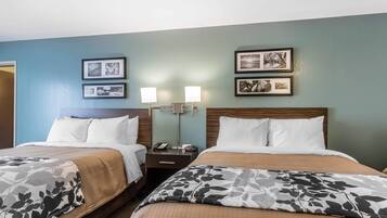 Quarto de hotel com duas camas, uma mesa de cabeceira com abajur e quadros nas paredes.