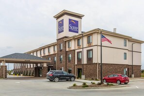 A Sleep Inn & Suites building with a parking lot, two cars parked, and an American flag.