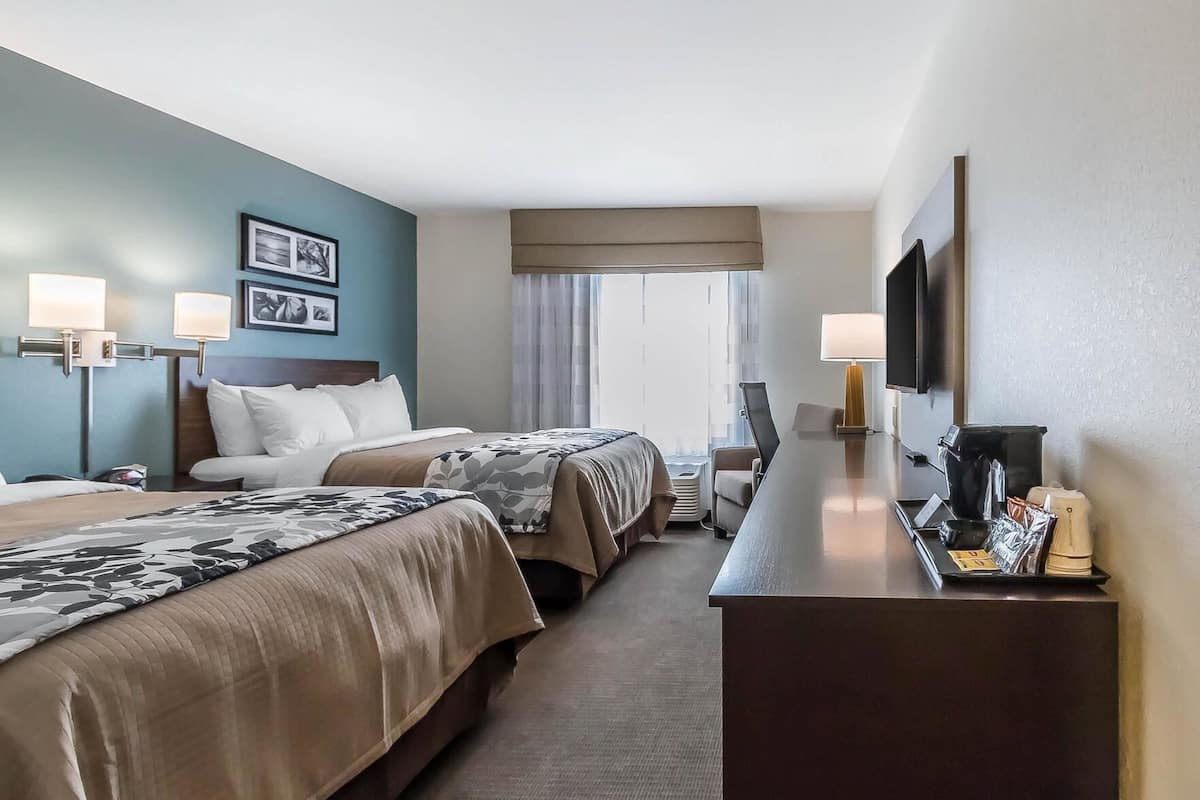 Quarto de hotel com duas camas, uma escrivaninha, televisão e uma janela com cortinas.