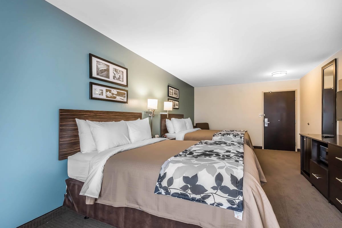 Quarto de hotel com duas camas, uma escrivaninha, cômoda e quadros na parede.