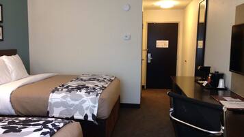 A hotel room with two beds, a desk, a chair, a coffee machine, and a door leading to another room.