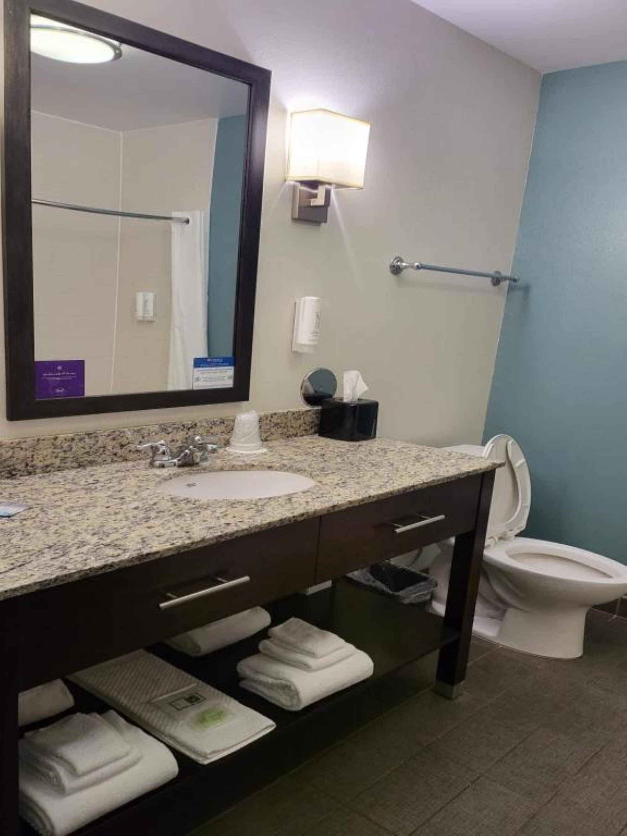 Un baño con lavamanos de encimera de granito, un espejo, toallero y un inodoro.