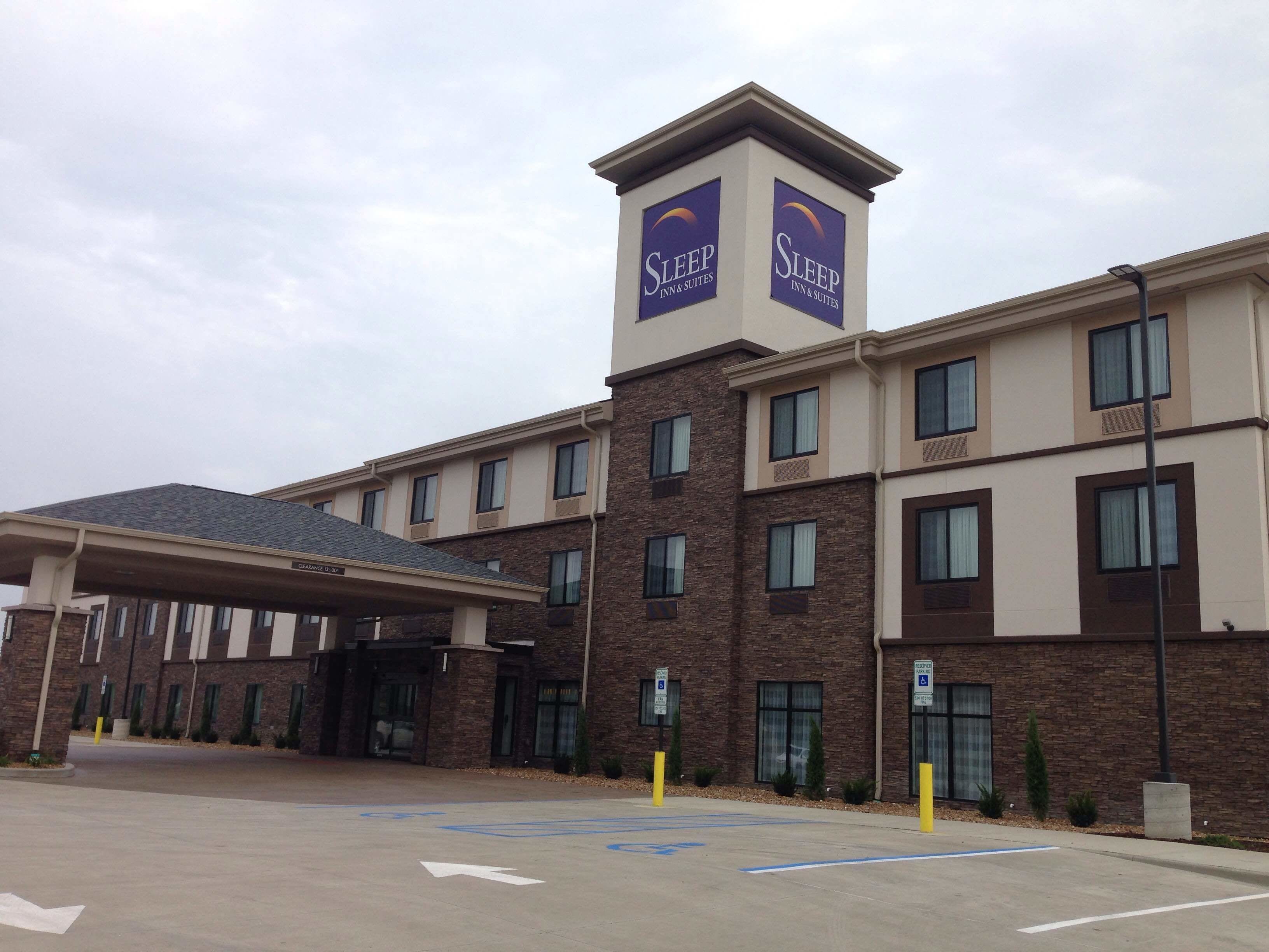 A Sleep Inn & Suites building with a covered entrance, multiple windows, and a parking area with handicapped accessibility signs.
