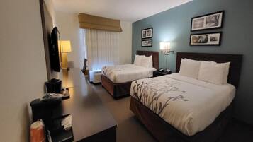 Une chambre d’hôtel avec deux lits, un bureau, une télévision et une fenêtre avec des rideaux.