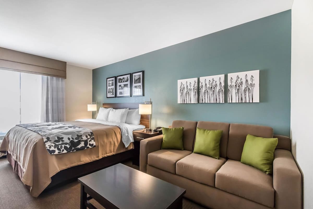 Quarto de hotel com cama, sofá, mesa de centro e obras de arte nas paredes.