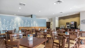 A restaurant with wooden tables and chairs, a blue wall with white floral patterns, and a counter with a coffee machine. - Sleep Inn & Suites O'Fallon MO - Technology Drive (O'Fallon)