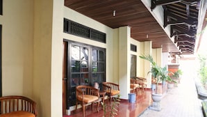 A covered outdoor seating area with wooden chairs and tables, potted plants, and a tiled floor. - RedDoorz @ Pratama Nusa Dua (Nusa Dua)