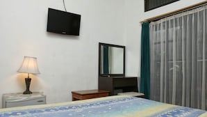 A hotel room with a bed, a desk, a lamp, a TV, a mirror, and a window with curtains. - RedDoorz @ Pratama Nusa Dua (Nusa Dua)