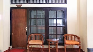A room with two wooden chairs, a small round table, and a large window with curtains. - RedDoorz @ Pratama Nusa Dua (Nusa Dua)