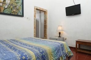 A bedroom with a bed, a TV mounted on the wall, a bedside lamp, and a wooden nightstand. - RedDoorz @ Pratama Nusa Dua (Nusa Dua)