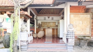 A traditional Balinese house with a tiled roof, a wooden porch, and a stone statue. - RedDoorz @ Pratama Nusa Dua (Nusa Dua)