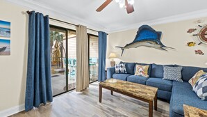 A living room with a blue sofa, wooden coffee table, and a ceiling fan. - Portside Resort by Panhandle Getaways (Panama City Beach)