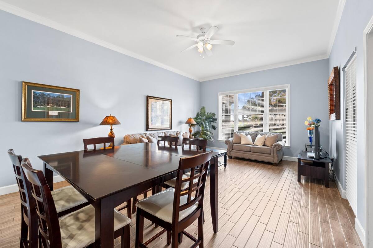 A spacious living room with a dining table, chairs, a sofa, and a ceiling fan.
