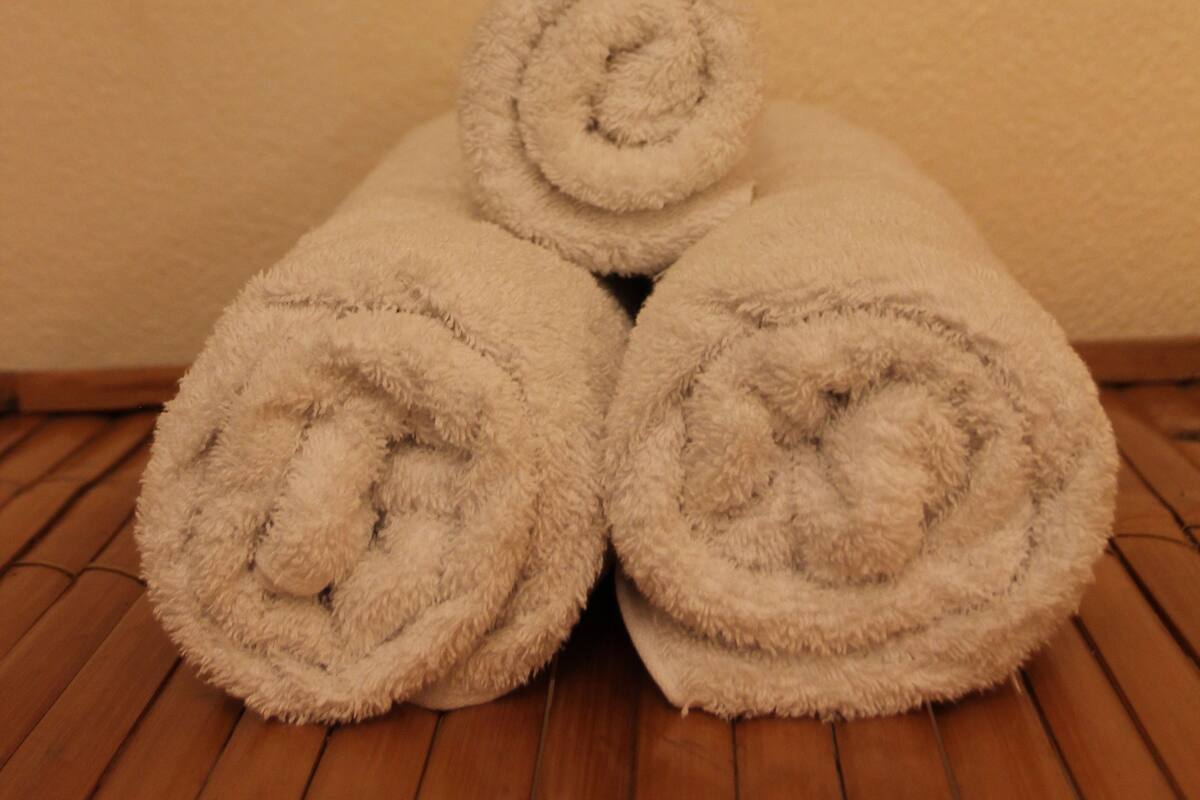Three rolled towels on a wooden floor with a wall behind them displaying a pattern of black fish.