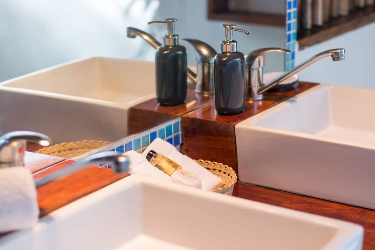 A bathroom with two sinks, each with a soap dispenser and a mirror above. There is a wooden tray with a towel and a bottle on it.