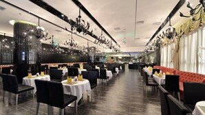 A restaurant with multiple tables and chairs, chandeliers, and a red sofa.