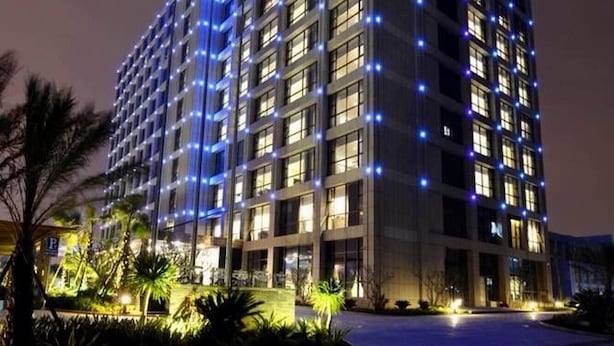 A multi-story hotel building with a modern design, featuring a series of balconies and a well-lit facade.