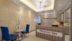 A reception area with a modern design, featuring a reception desk, two blue chairs, a small table, and a decorative chandelier.