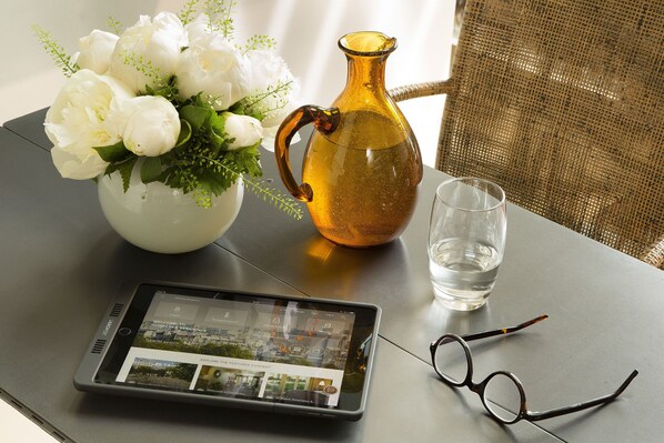 A tablet displaying a hotel interior, a vase with white flowers, a golden vase, and a clear glass of water on a table. - Goralska Residences Paris Bastille (PARIS)