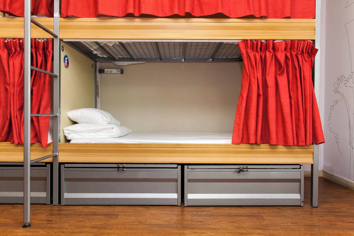 A bunk bed with red curtains, a ladder, and two drawers under the bed.