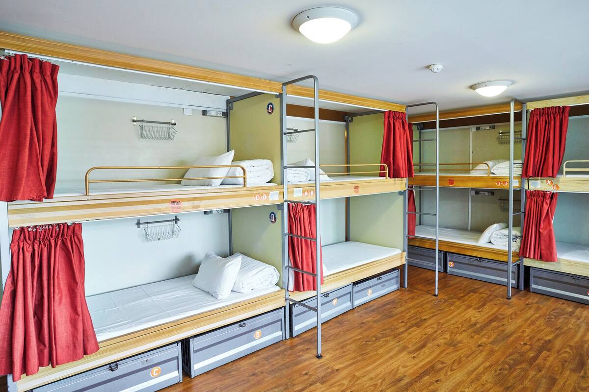 A dormitory with bunk beds, each with a small shelf and a red curtain.