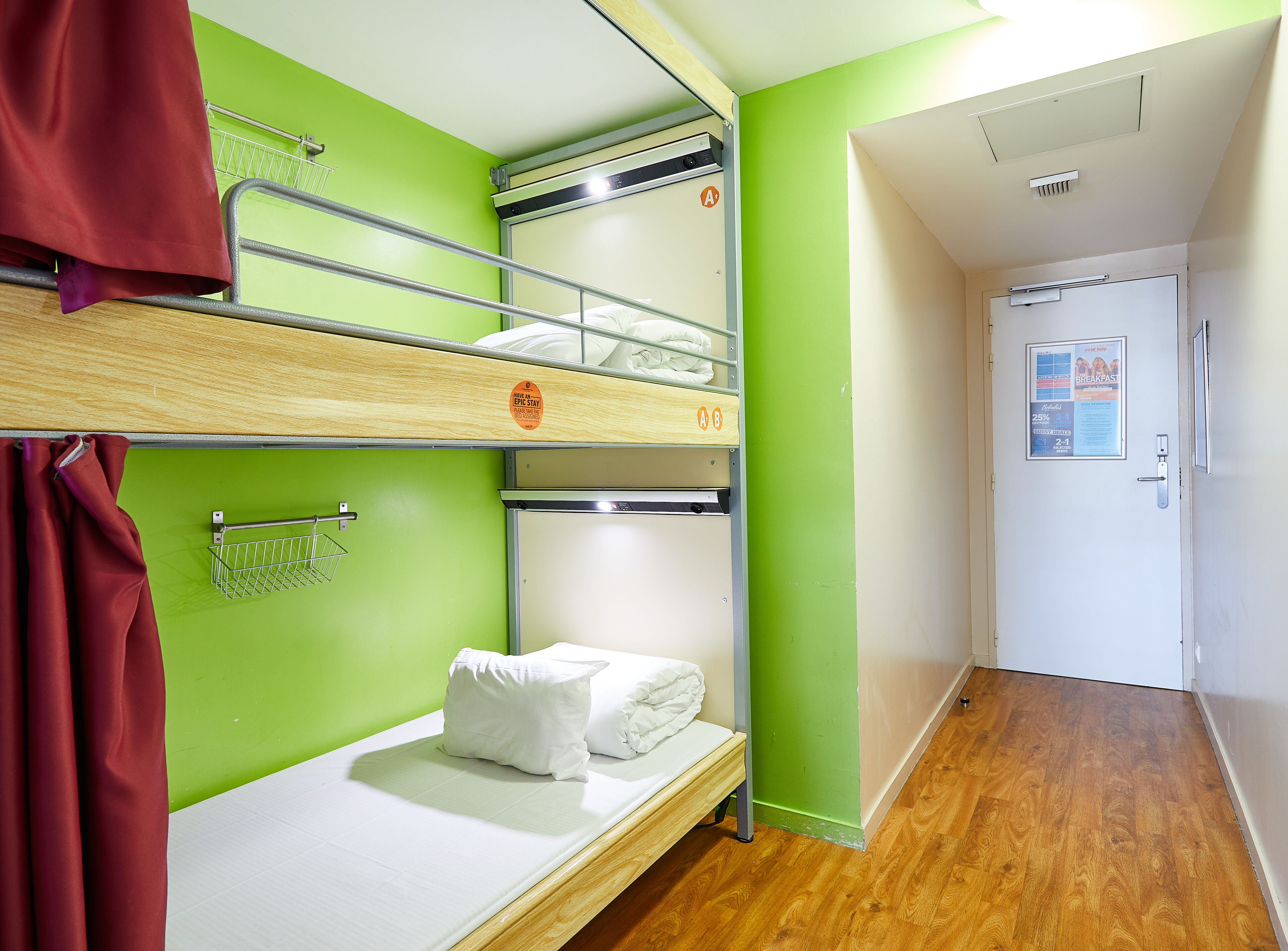 Habitación con literas, una pared verde, piso de madera y una puerta con un cartel.