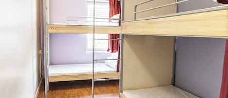 Quarto com beliche, piso de madeira, janela com cortinas e escada de metal.