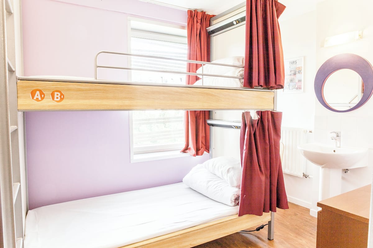 A bunk bed with a window, a sink, and a mirror in a room with light purple walls.