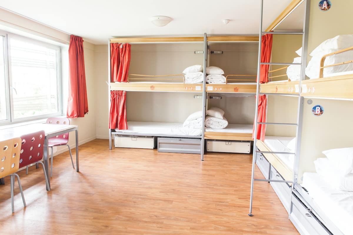 A bunk room with wooden bunk beds, a desk with chairs, and a window with curtains.