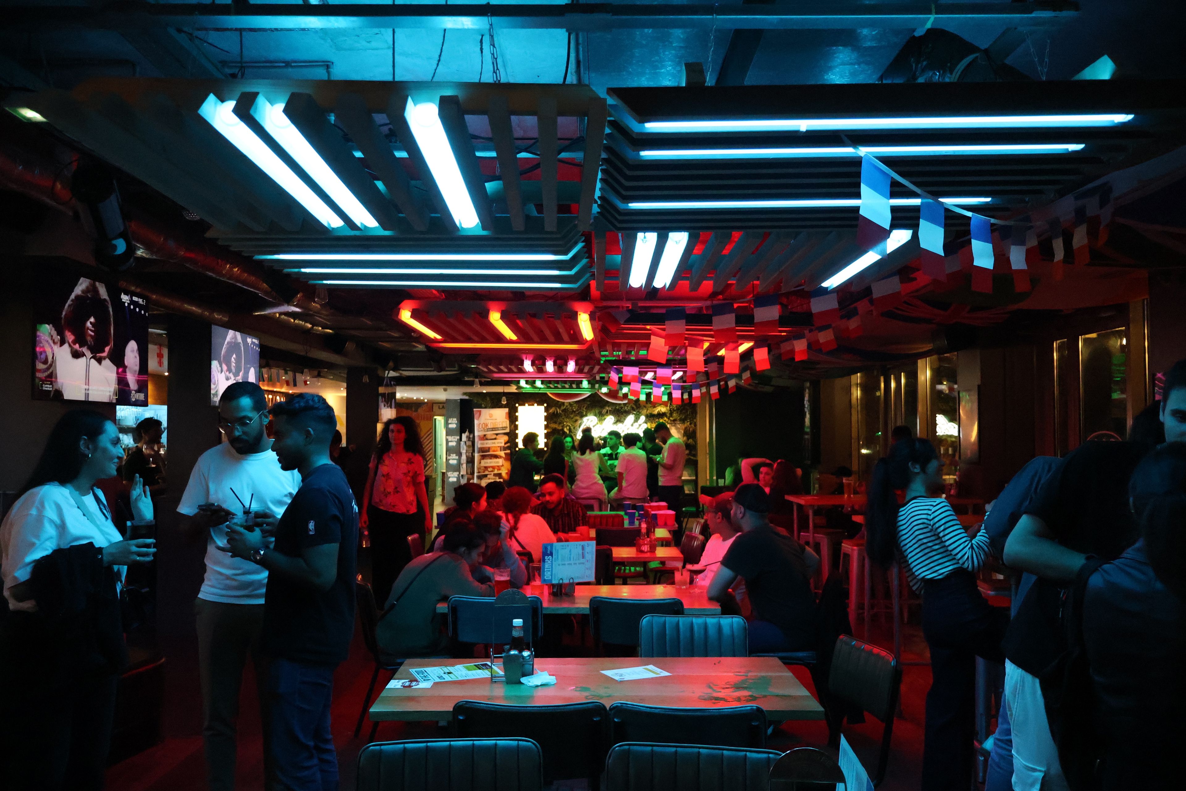 Un restaurant avec de nombreuses tables et chaises, des néons au plafond et une foule de clients.