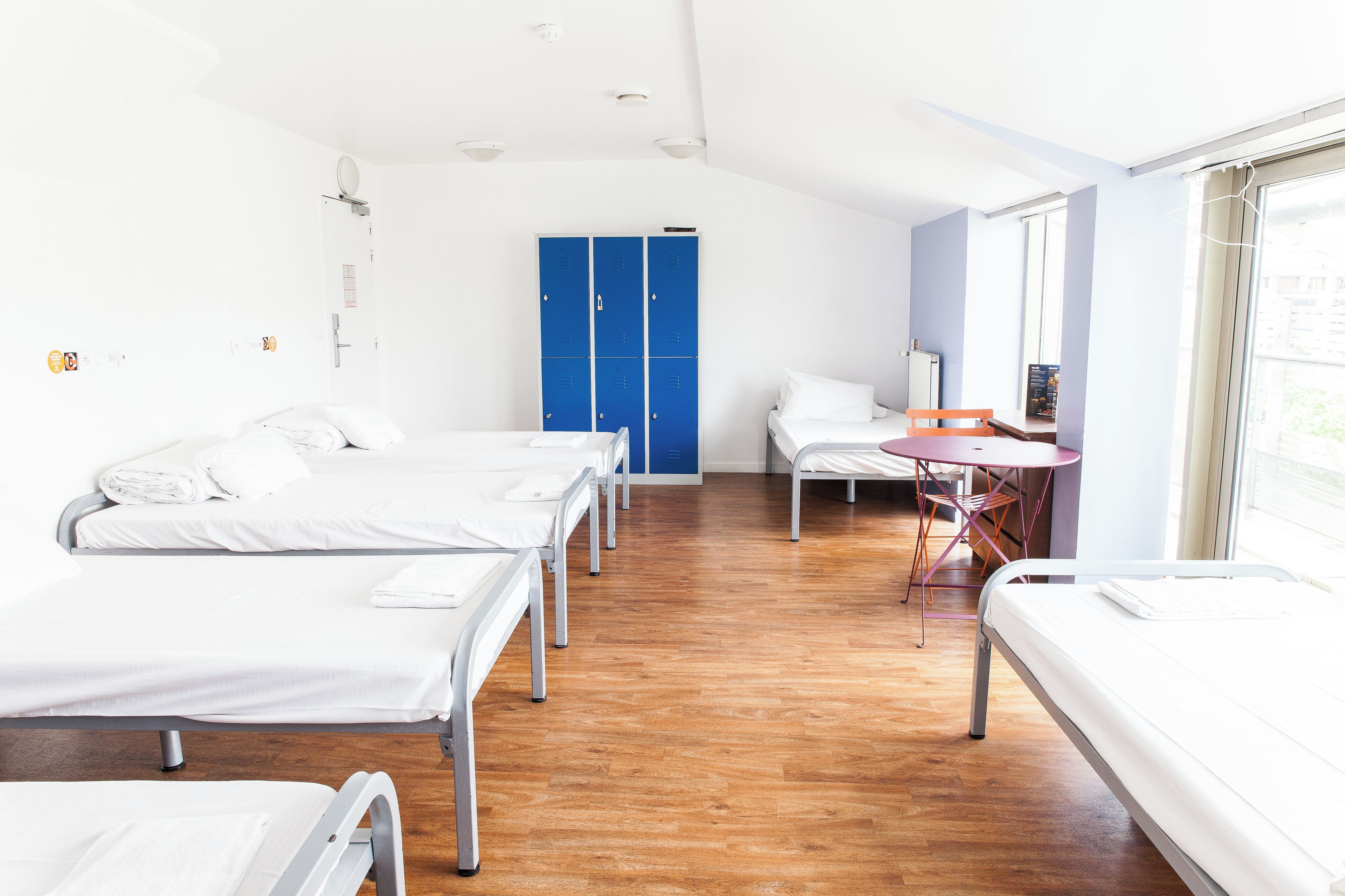 Habitación de hotel con cuatro camas individuales, una mesita pequeña y un armario azul.