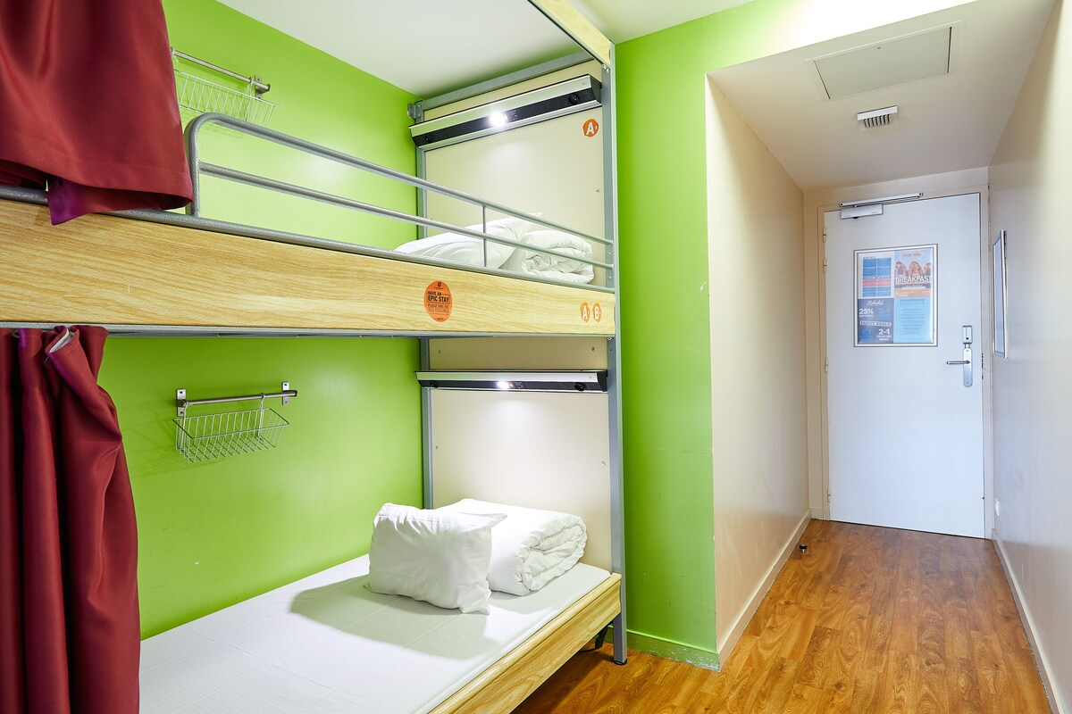 A bunk bed room with a green wall, a white door with a poster, and a wooden floor.
