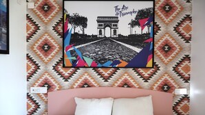 A bed with a pink headboard, a wall with a geometric patterned wallpaper, and a framed picture of the Arc de Triomphe. - St. Christophers Paris Canal (Paris)