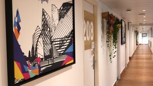 A hallway with a framed artwork of the Louis Vuitton Foundation, a door labeled '208', and a wall-mounted plant. - St. Christophers Paris Canal (Paris)