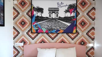 A bed with a pink headboard, a wall with a geometric patterned wallpaper, and a framed picture of the Arc de Triomphe.