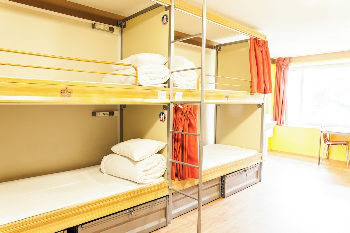 A bunk bed room with a window, a chair, and a small table.