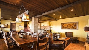 Un vaste espace dédié à la salle à manger, avec une grande table et des chaises en bois, une cheminée et un plafond rustique.