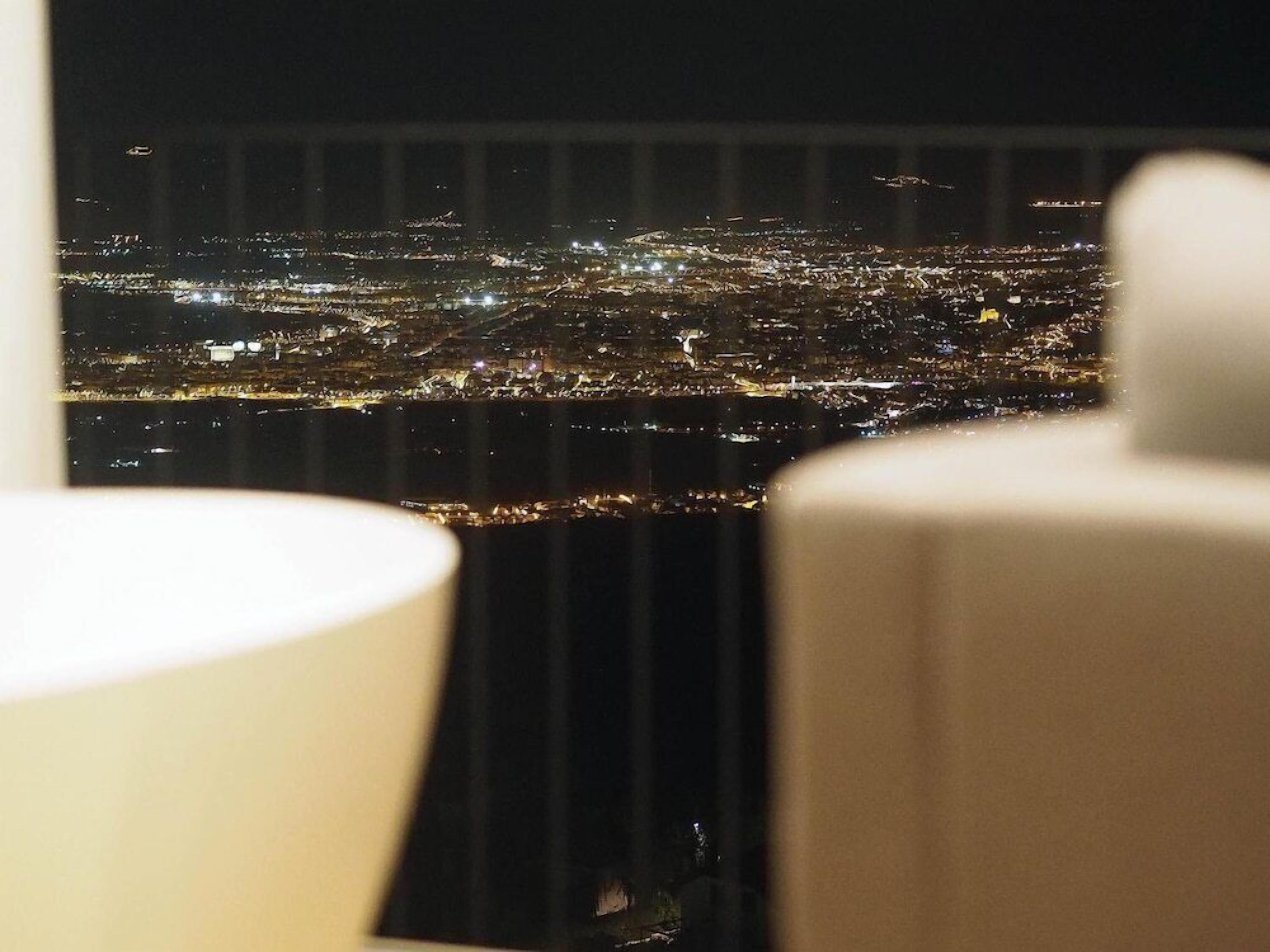 Vista nocturna d'una ciutat des d'un punt elevat, probablement des d'una habitació d'hotel.