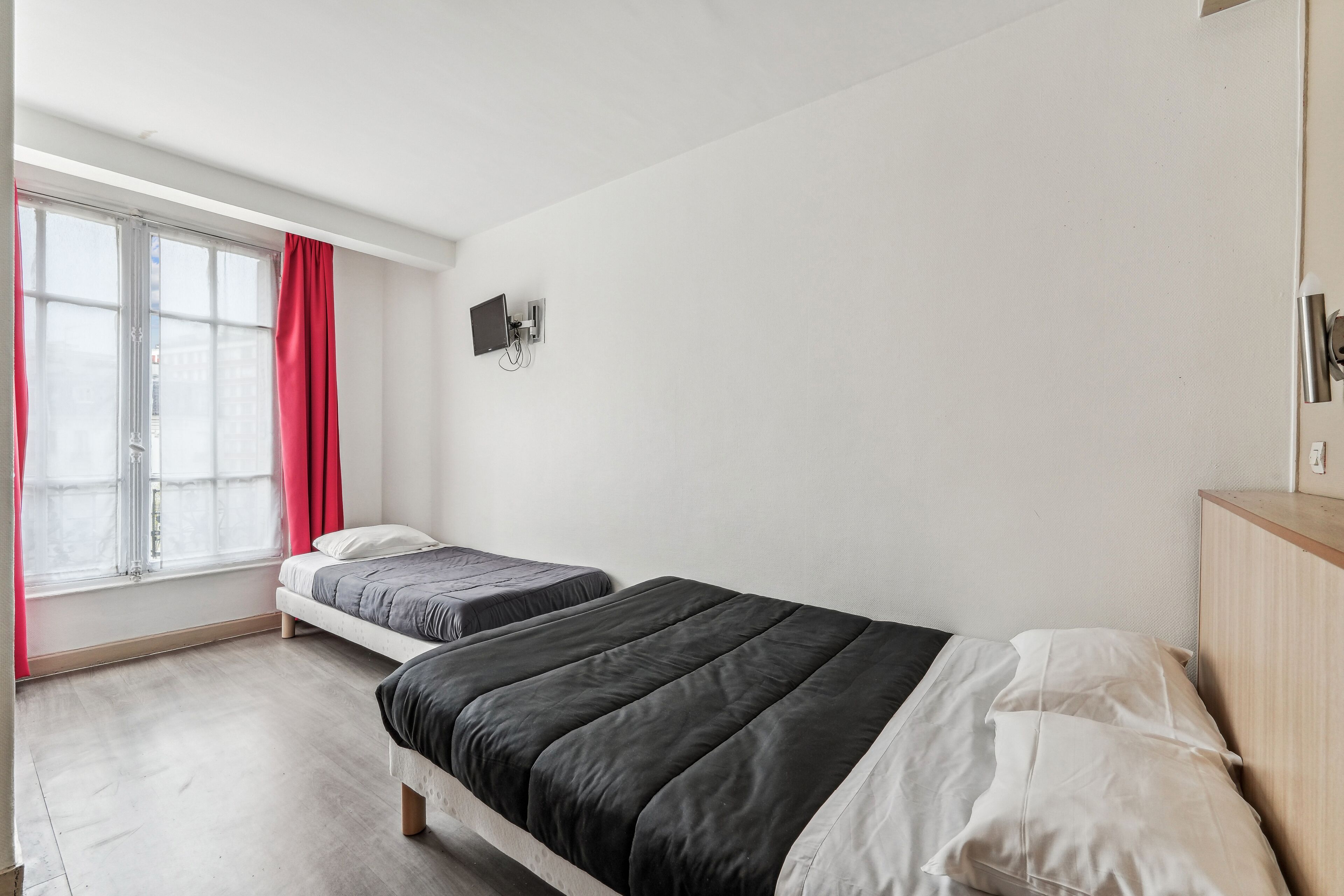 Een slaapkamer met twee bedden, een raam met rode gordijnen, een tv aan de muur en een houten kast.