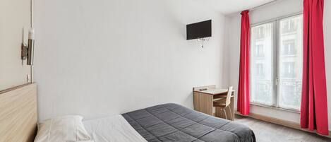 A bedroom with a bed, a desk, and a TV mounted on the wall.