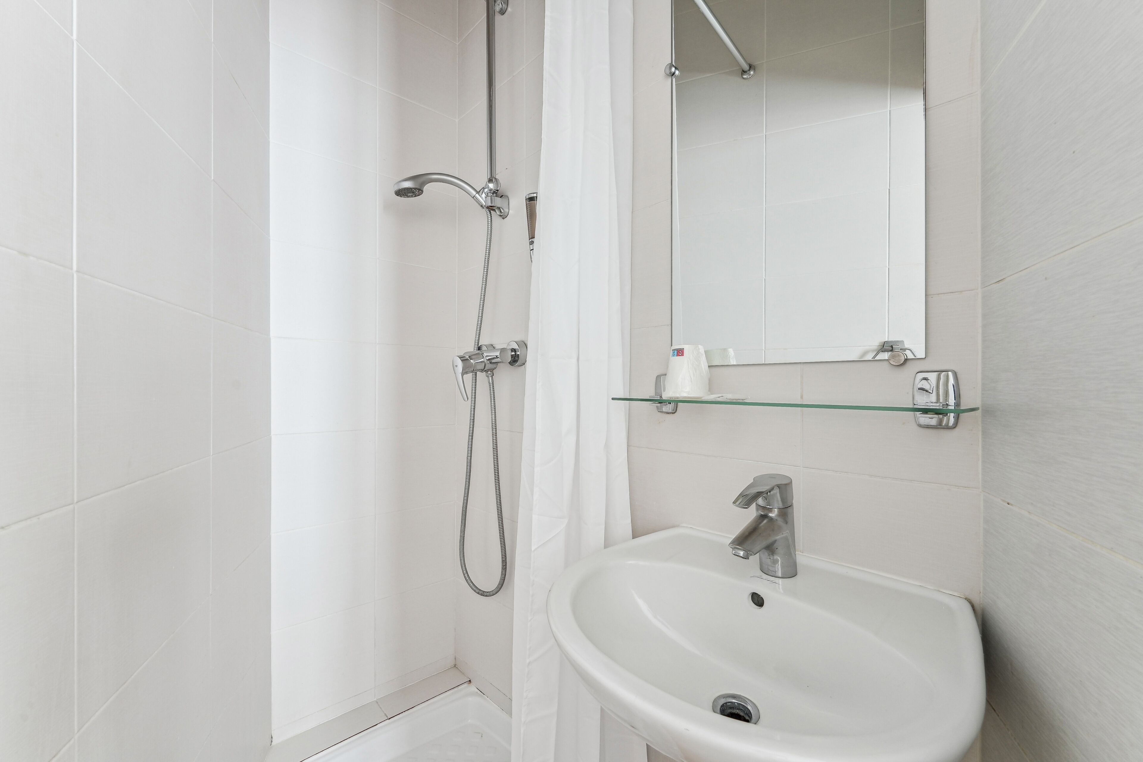 A modern bathroom with a shower, a glass shelf above the sink, and a mirror.