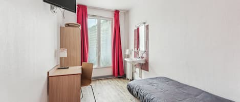 Une chambre à coucher comprenant un lit, un bureau, une chaise, un téléviseur fixé au mur, une fenêtre avec des rideaux et un lavabo.