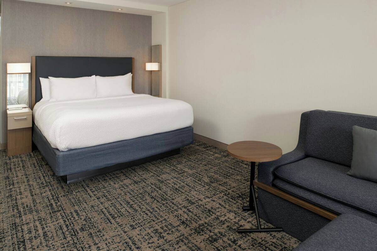 Ett hotellrum med en stor säng, ett litet runt bord och en soffa.