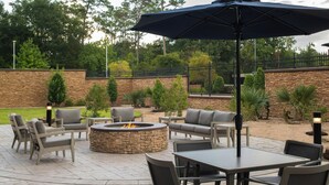 Un espace extérieur aménagé en terrasse, avec un sol en pierre, un foyer et du mobilier d’extérieur comprenant des chaises et des tables.