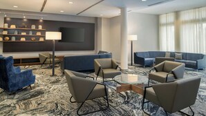 Un hall d’hôtel moderne doté d’un grand espace salon, d’un téléviseur à écran plat fixé au mur et d’un tapis à motifs.