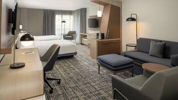 A modern hotel room with a bed, a sofa, a desk, a TV, and a coffee machine.