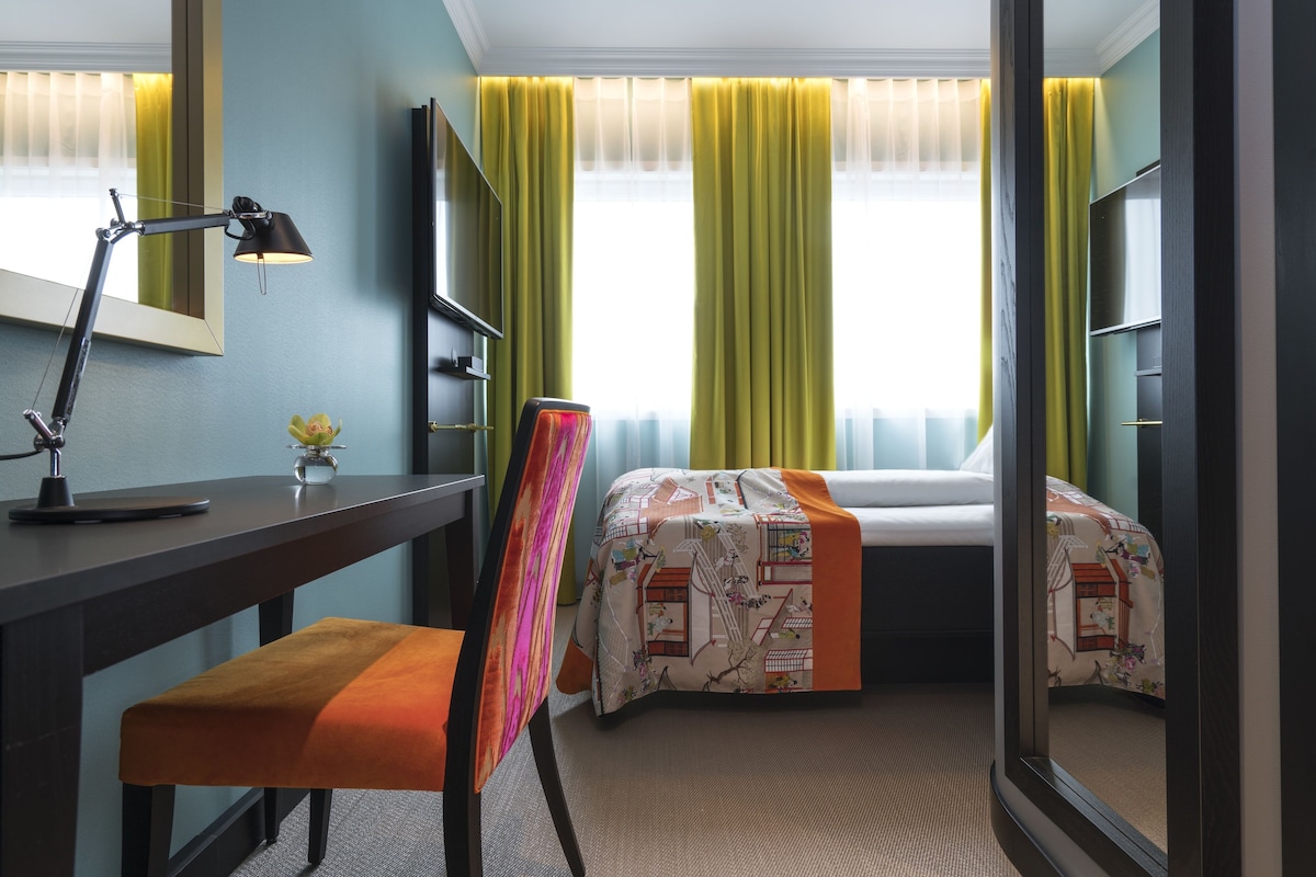 A hotel room with a desk, chair, bed, and a large mirror.